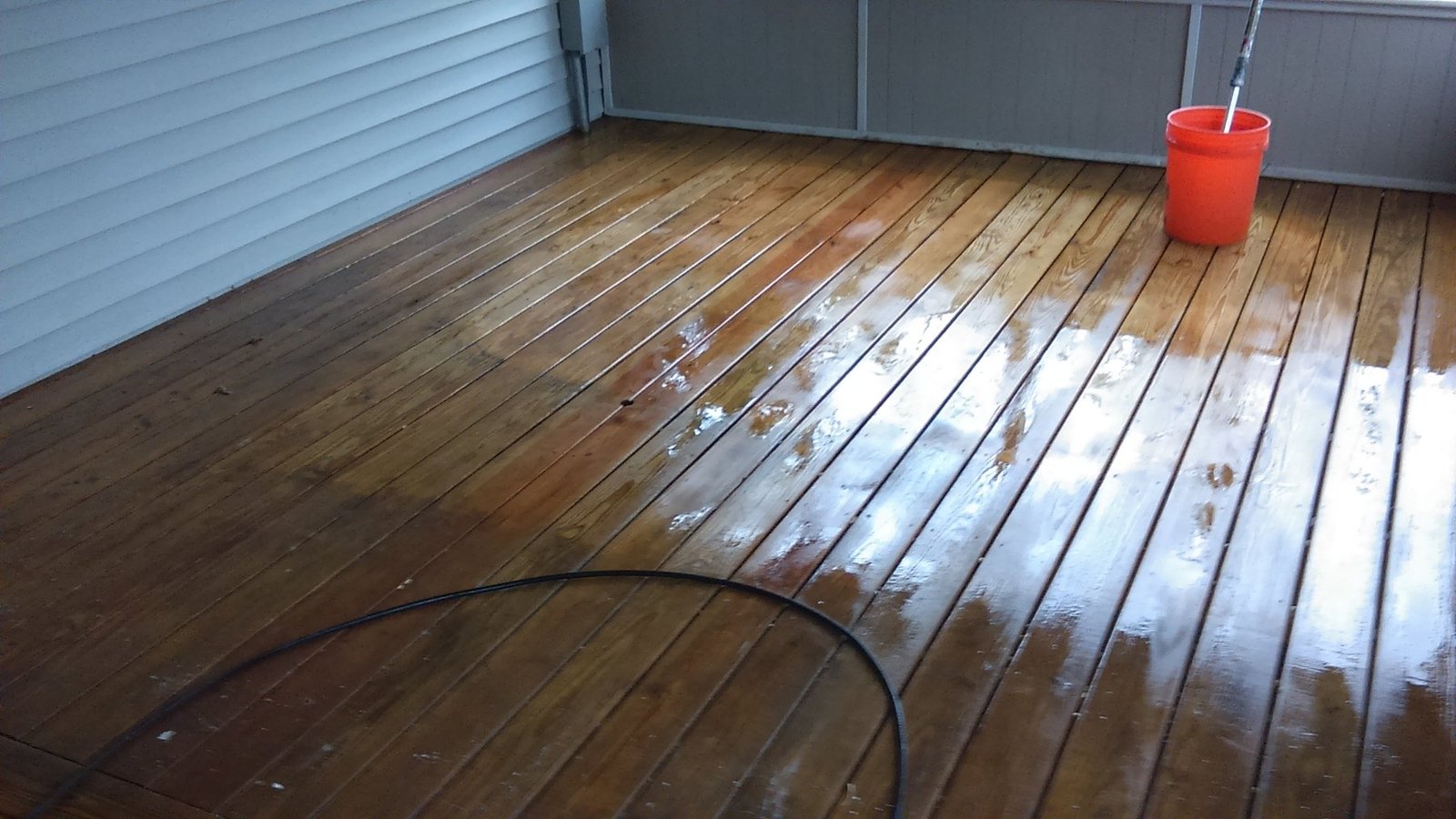 Wet wood deck during cleaning work with a hose and bucket visible